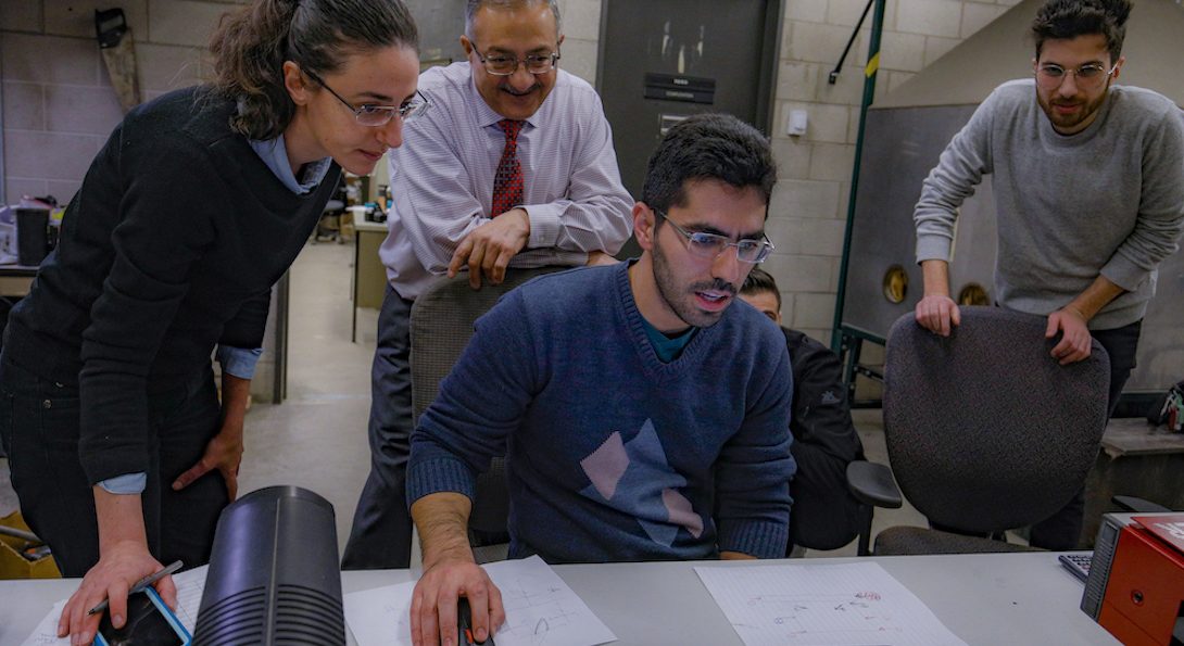 Three doctoral students work in a lab with Professor Mohsen Issa